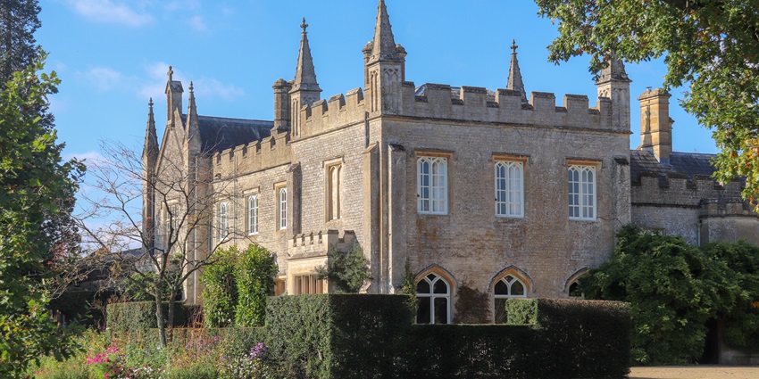 View of a Gothic-style manor house and garden in Huntingdon under a clear blue sky.