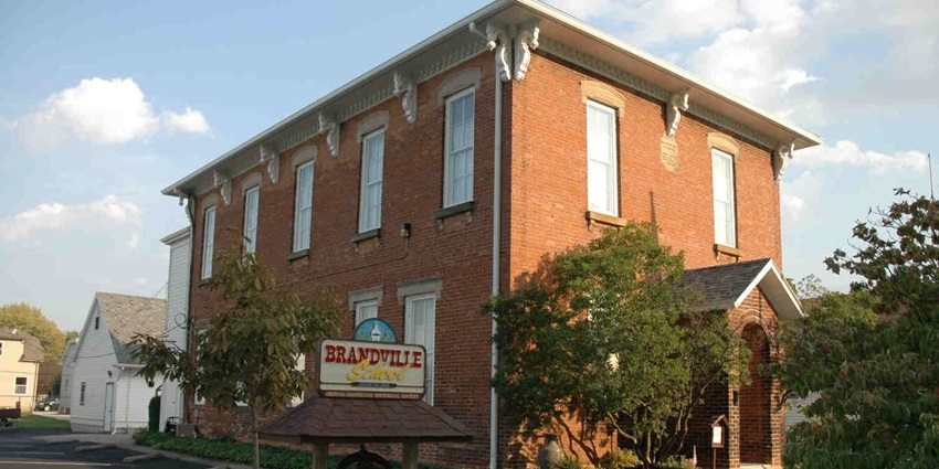 Brandville school museum in Oregon with a big bell, sign boards on top of the bell and greenery.