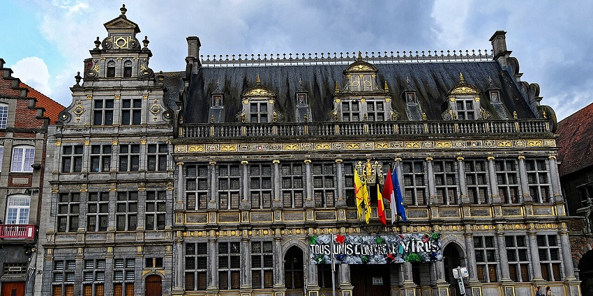 Ornate historic buildings with golden details, flags, and planters in a cobbled square.