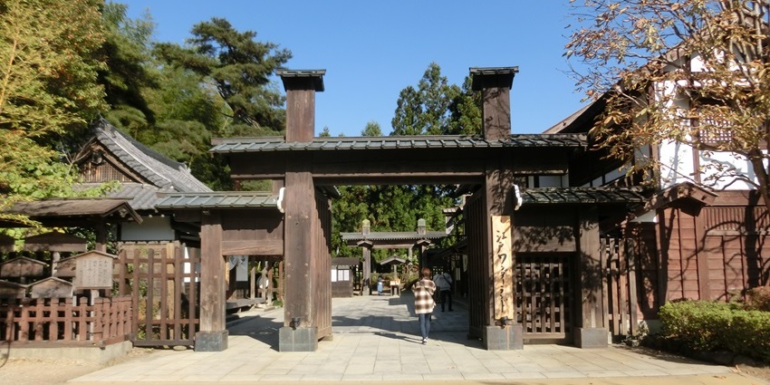 Traditional wooden gate leading into a courtyard lined with trees and historic buildings.