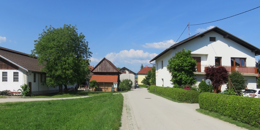 Peaceful village streets lined with houses, green lawns, and trees under a clear blue sky.