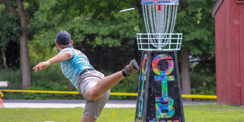 Person playing disc golf outdoors, throwing a disc toward the target basket.
