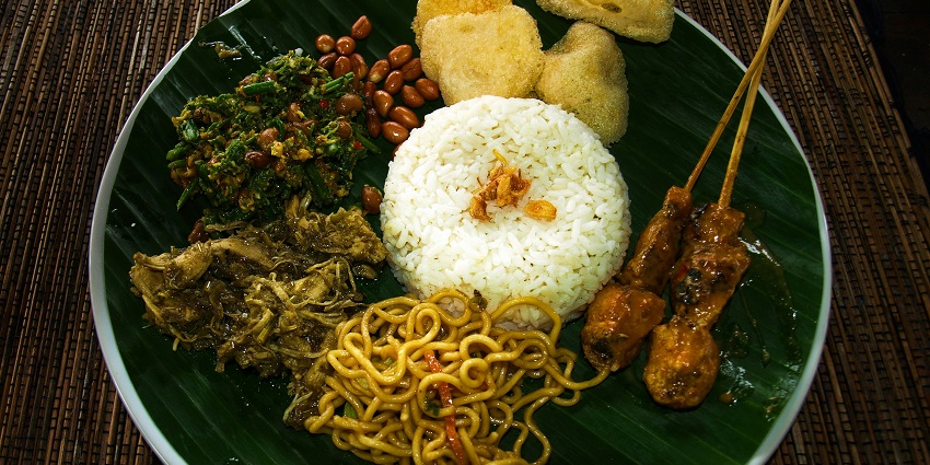 A colorful Bali platter featuring rice, chicken, and noodles served on a plate.
