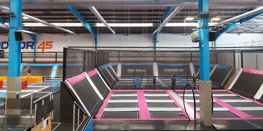 Inside a trampoline park with black & pink trampolines, distant kids jumping and white lights, one of the best things to do in Plymouth MN.
