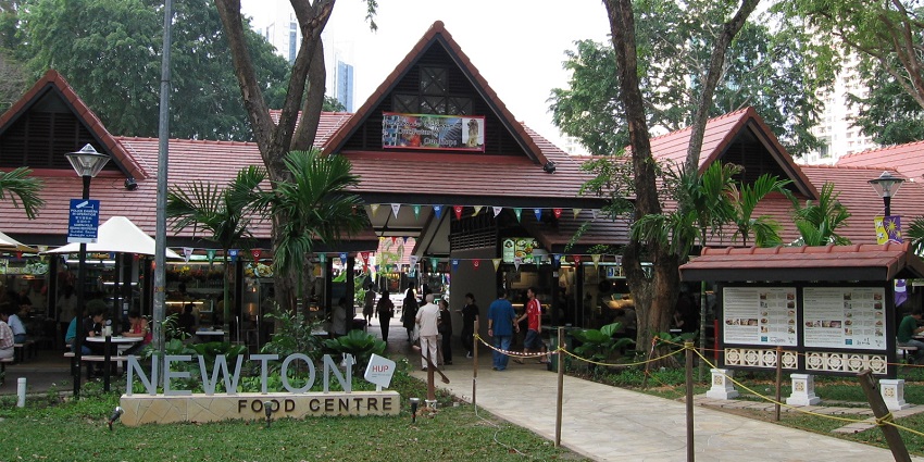 An open-air food court at Newton Food Centre with diners seated near brightly lit stalls.