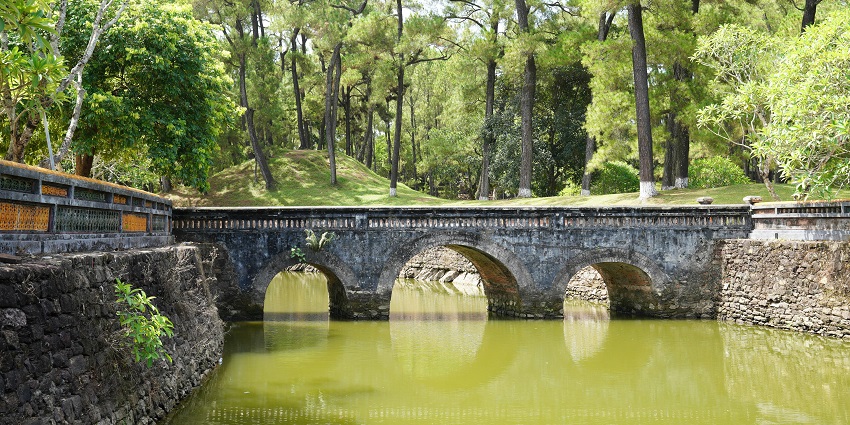 Panoramic view of the Four Seasons Centre with a lake, trees, and a stone bridge.