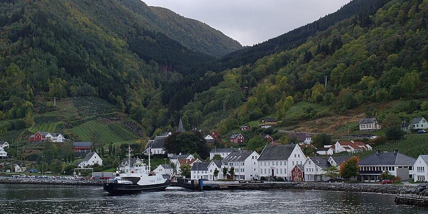 Utne in Norway with a boat on the water, white architectural buildings and green mountains.