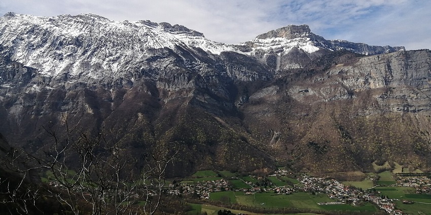 Snow-dusted alpine cliffs above a green valley, one of the beautiful places to visit near Lyon.