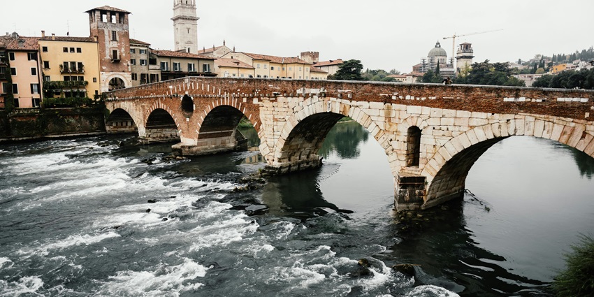 Verona, with an old architectural bridge over a river, traditional Italian buildings, and houses.