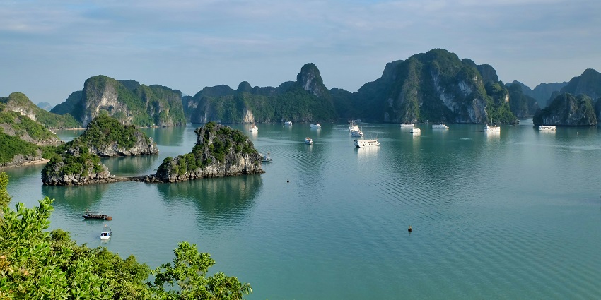 The scenic limestone islands of Halong Bay rise from emerald waters, one of the amazing places to visit near Thailand.
