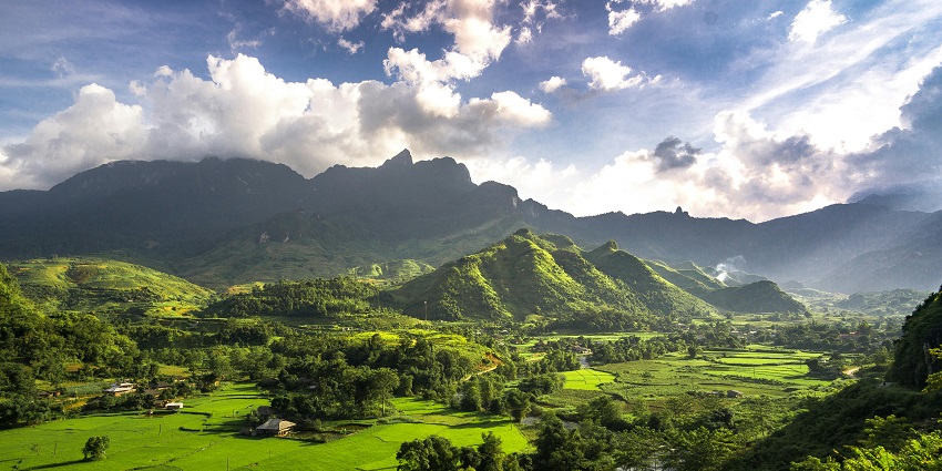 Hà Giang in Vietnam with green grass fields, trees, distant buildings and mountains.
