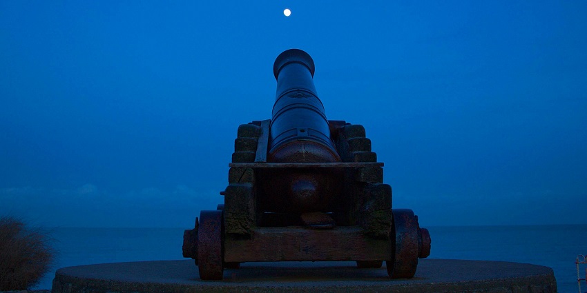 A huge colonial-era style cannon on a pedestal aimed towards the sky at nighttime.