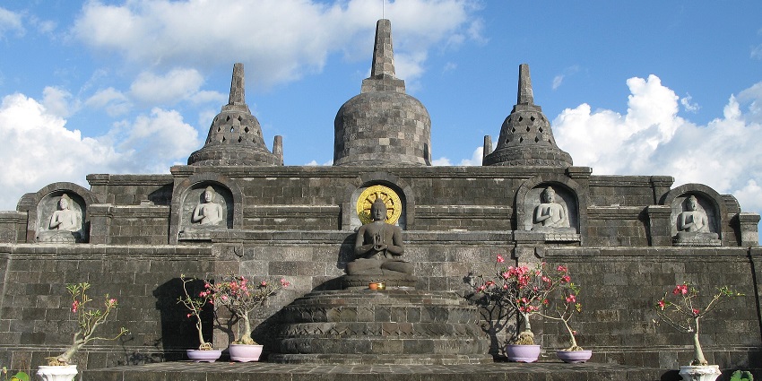 Brahmavihara Arama temple structures with stone stupas under a clear blue Balinese sky.
