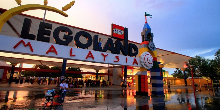 Entrance of Legoland Malaysia Resort at dusk with colourful Lego tower and wet ground.
