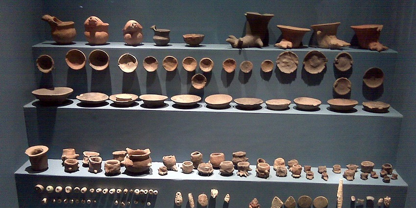 Inside a museum with multiple old antique pieces on the grey surface on display behind glass.
