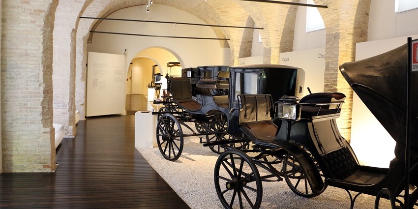 Black carriages displayed in a vaulted stone hall at Macerata’s Museo delle Carrozze.