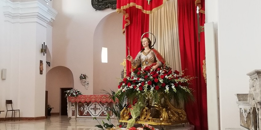 Marble statue of Saint Cristina standing beside the stone wall of Santa Maria a Mare church.