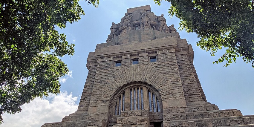 The towering Völkerschlachtdenkmal in Leipzig is surrounded by greenery on a clear sunny day.
