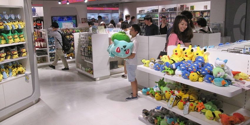 Merchandise shelves inside Mega Tokyo Pokémon Centre with plush toys and themed products.
