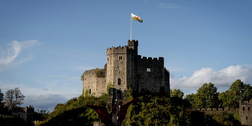 A Castle on top of a mountain with stairs leading to the structure and a flag in Cardiff.