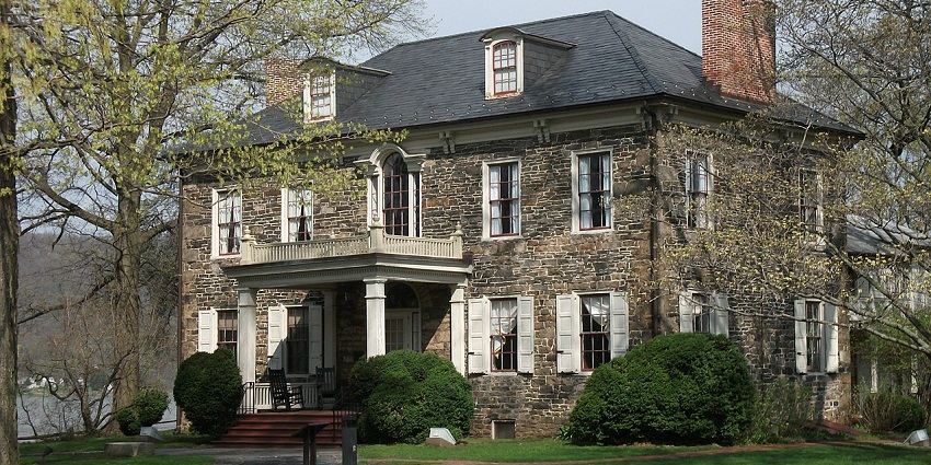 The two-story Fort Hunter mansion is surrounded by trees and shrubs, enclosed by a lawn.