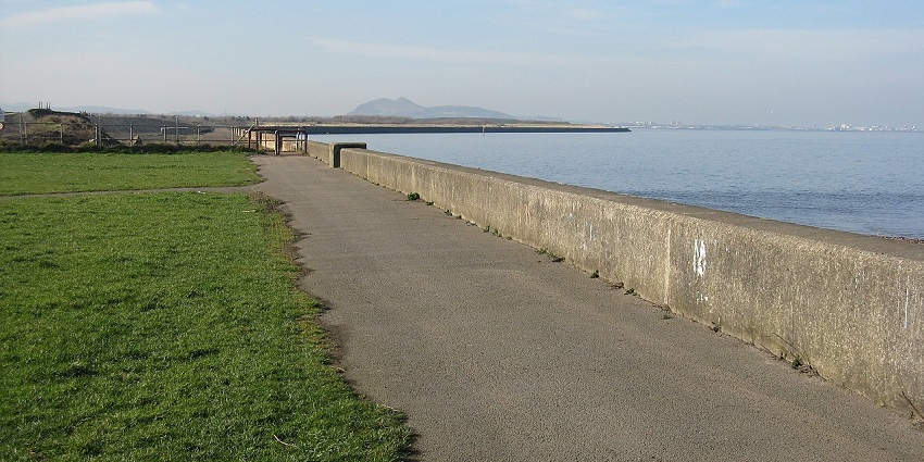Walking path along the John Muir Way with greenery on one side and a lake on the other.