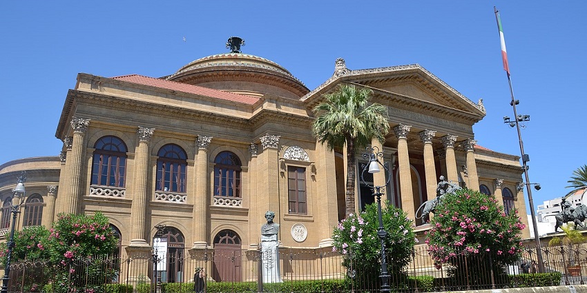 Teatro Massimo in Palermo with an Italian architectural building, with a tall Italian flag, and trees.
