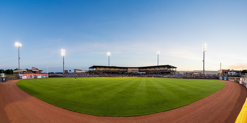Trustman Park in Mississippi with finely cut green grass, tall stadium lights and distant sitting chairs.