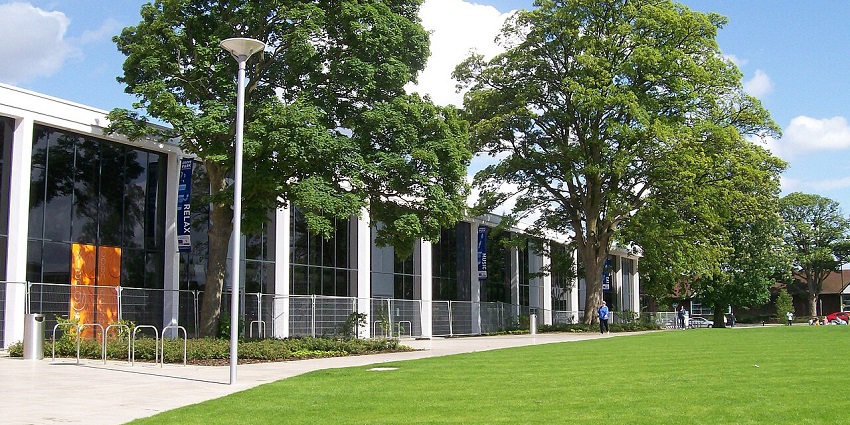 Theatre with a simple facade, surrounded by green lawns and trees in a natural setting.