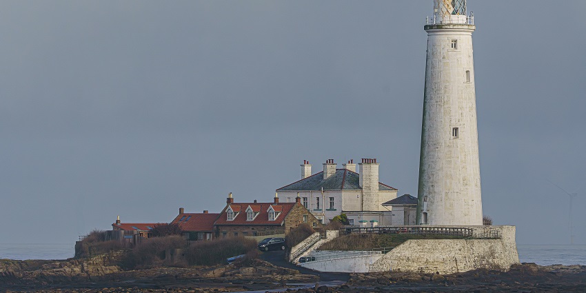 Small stone lighthouse building standing beside the calm waterfront promenade.