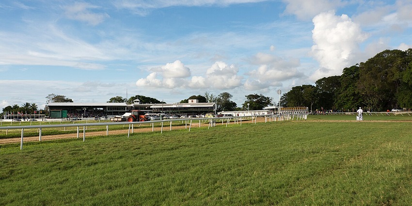 Garrison Savannah in Barbados with horse racing tracks, fencing, a man standing and greenery.
