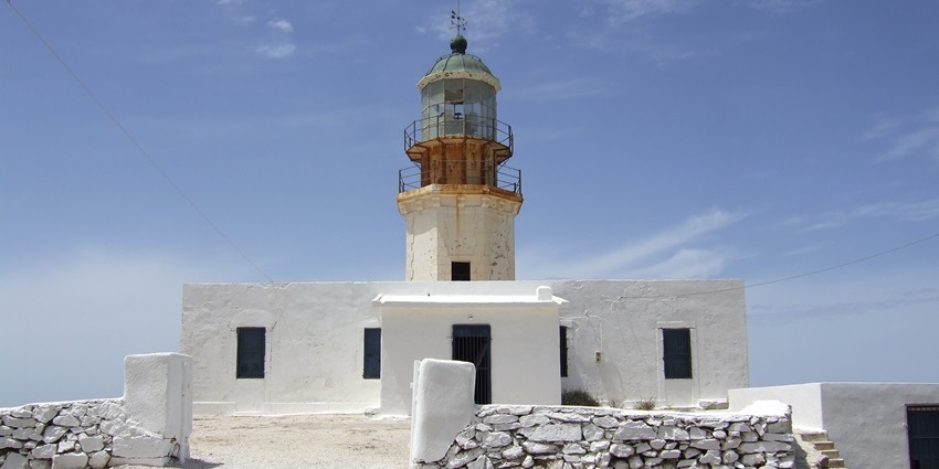 Old white lighthouse with a weathered tower on a rocky hilltop under a partly cloudy sky.
