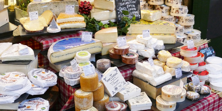 Assorted cheeses on display at a market stall with different shapes and colors.
