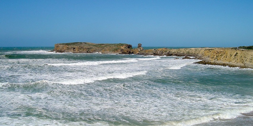 Papôa Peninsula in Peniche with high tide waves of the water and distant small rocky cliffs.