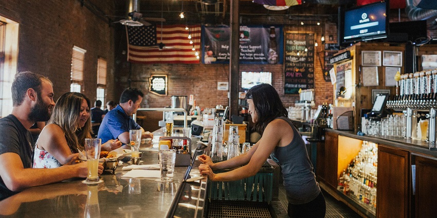 The interior of a bar with dim lights, where people are enjoying drinks at the counter.