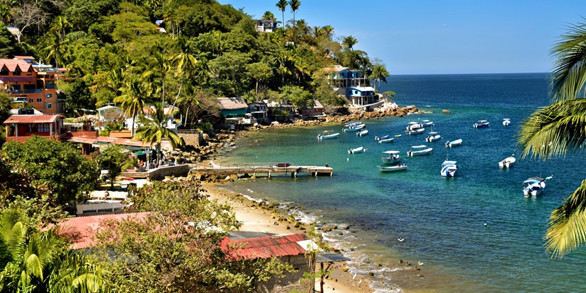 Yelapa beach with several boats in the sea and buildings hidden in the greenery of the beach, one of the places to visit near Puerto Vallarta.