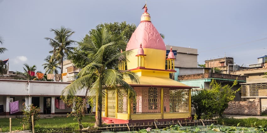 A peaceful riverside view at Achipur with lush greenery and calm waters under a clear sky.
