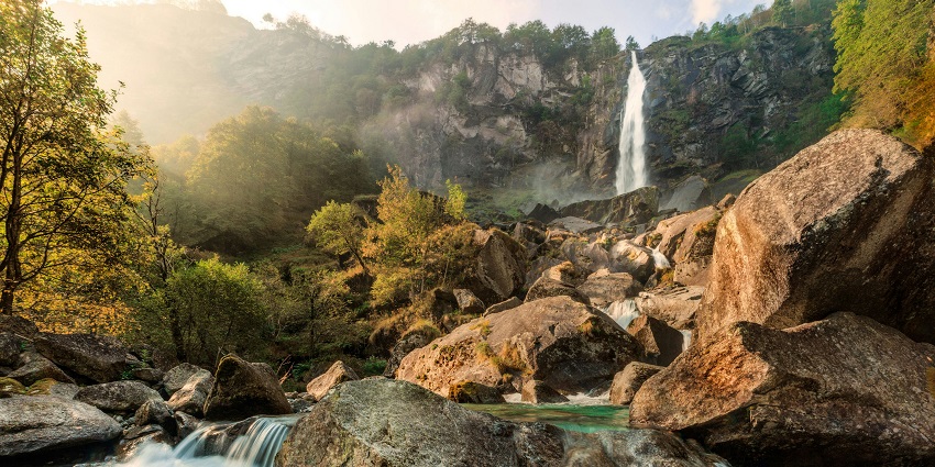 Adai Waterfall cascading down rocky cliffs surrounded by lush green forest.