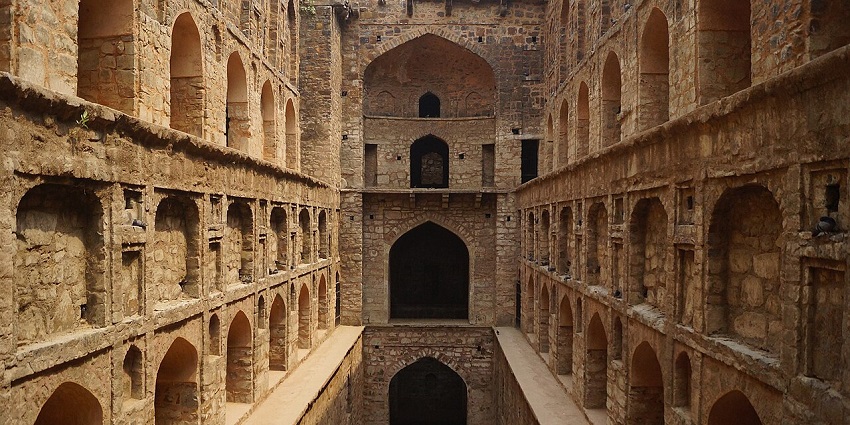 Ancient stepwell with layered levels and symmetrical stone archways on both sides.
