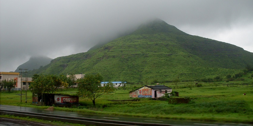 A wide view of green mountains with cloudy hazy sky and village houses in front