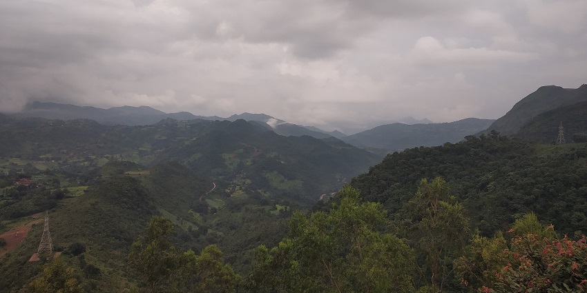 Hilly tracts of green running into the distance under dense grey clouds and soft sunlight.