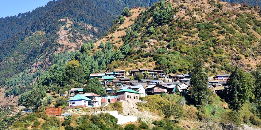 Mountain village with scattered houses on a green hillside under clear blue skies.
