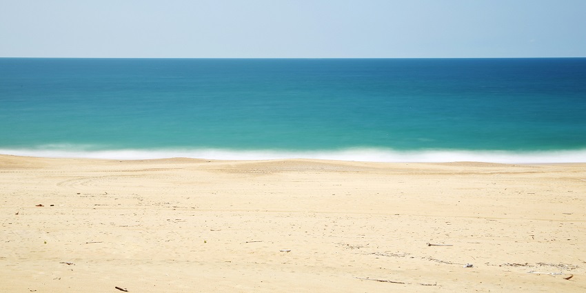 Bakkhali Beach with its sandy shore, gentle waves, and a calm, cloudy sky above.
