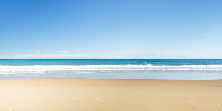 Wide view of Bakkhali beach with calm sea and sandy shore under a clear sky.