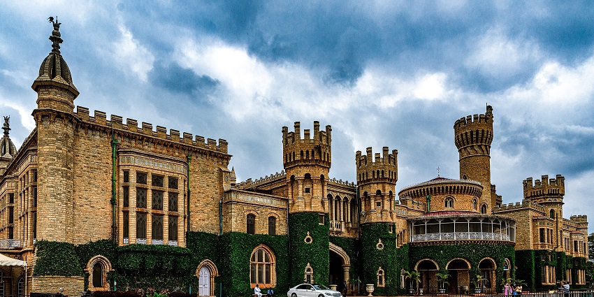 Bangalore Palace with traditional architecture, a white vehicle parked and people visiting.
