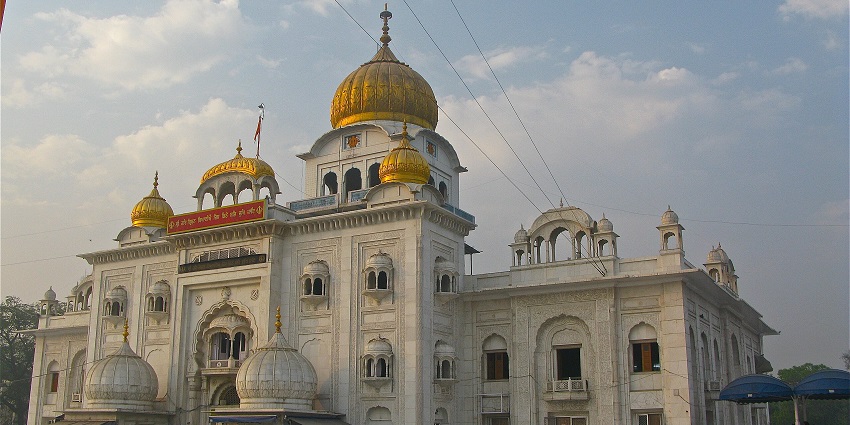 Gurudwara Bangla Sahib in Delhi with golden domes, white marble walls, and visitors.
