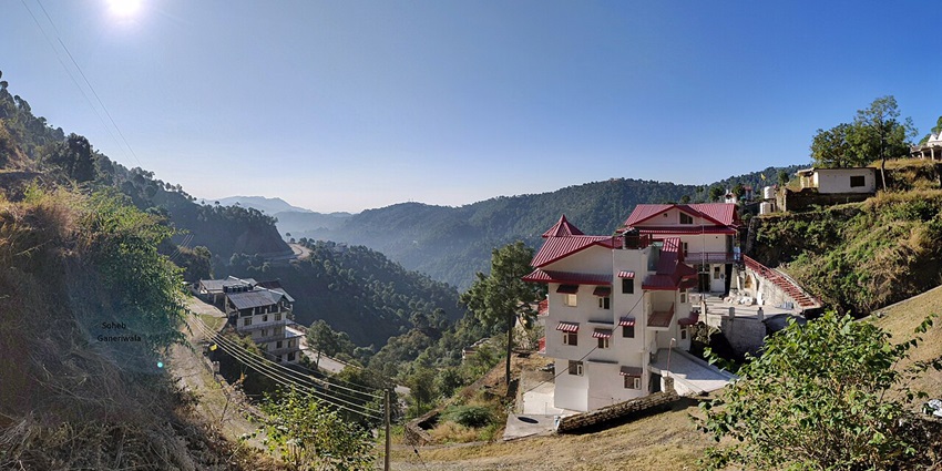Sunny view of Barog Valley with white hillside homes, lush green slopes, and pine forests.