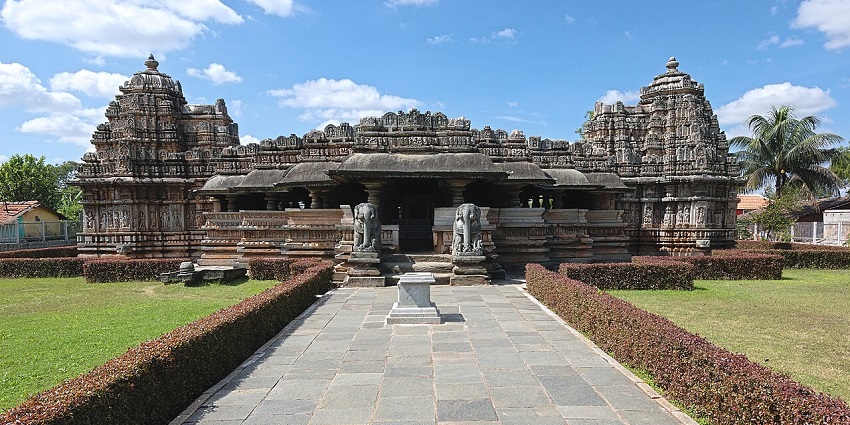 Symmetrical stone temple with ornate towers, set in a manicured green garden pathway.