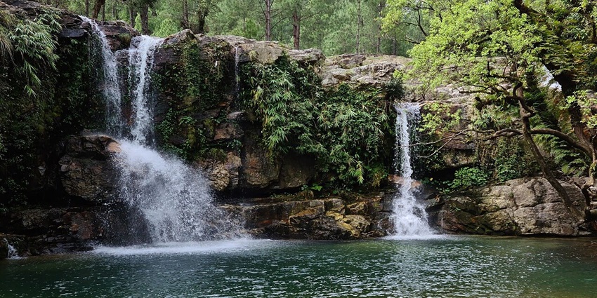 Tunkhola waterfall in Berinag, with water flowing on the uneven rocky surface and greenery.