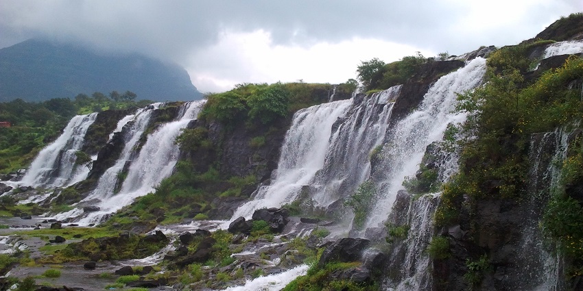 Wide waterfalls cascading over rocky ledges with mist rising under thick cloudy skies.